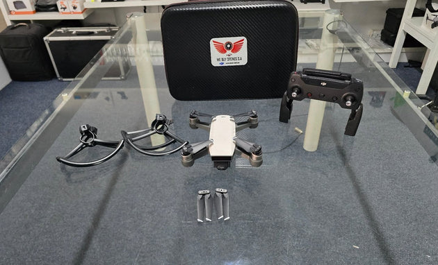 Pre-Owned DJI Spark drone with controller, props, prop guards, and carrying case on glass table.