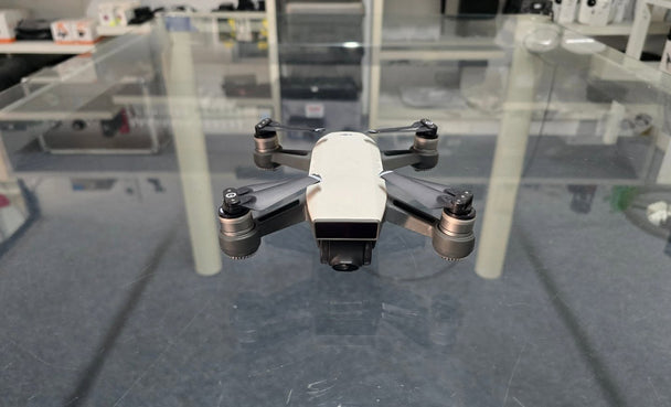 Pre-Owned DJI Spark drone displayed on a glass surface with props and camera visible.