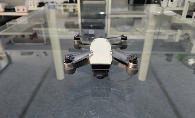 Pre-Owned DJI Spark drone displayed on a glass surface with props and camera visible.